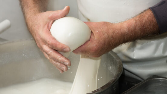 This photo shows a man's hands pulling fresh mozzarella out of a mixing bowl and balling it up.