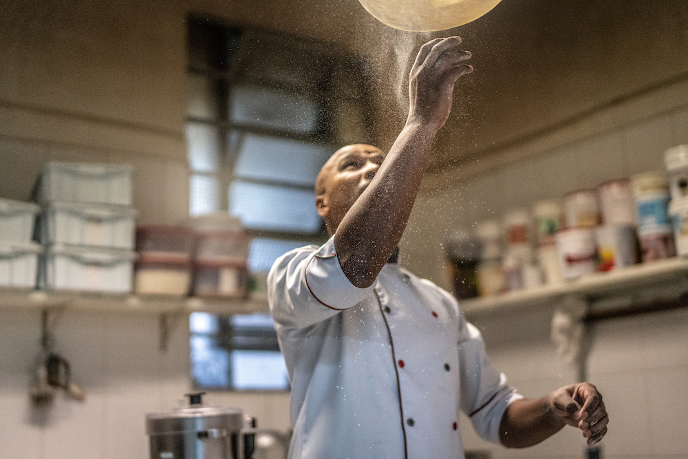 a black chef tosses pizza dough in a pizza kitchen