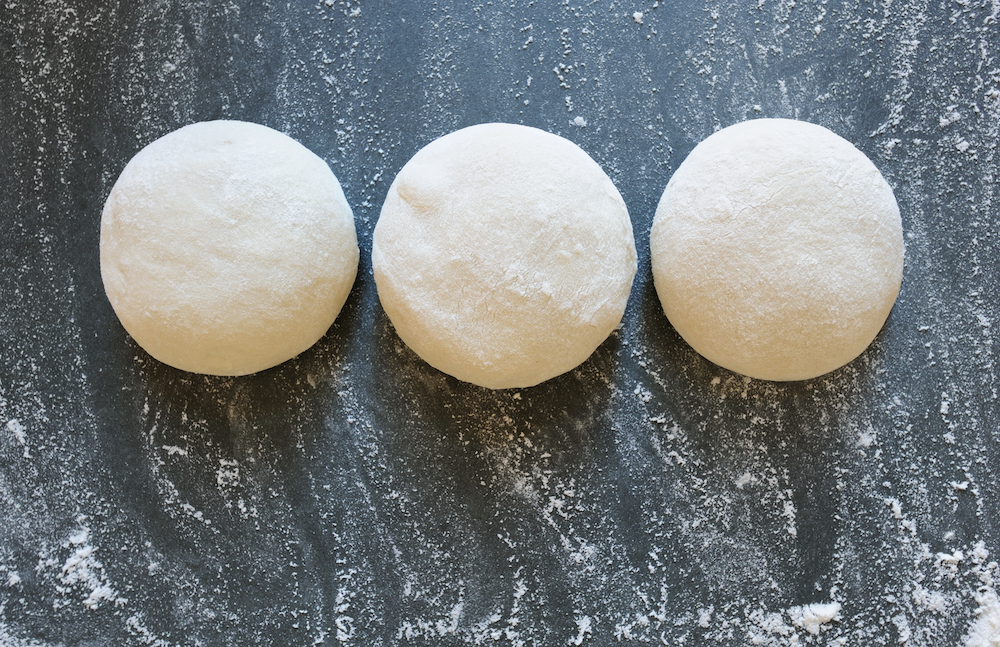 This photo shows a line of three dough balls on a dark gray table.