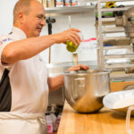 This photo shows John Arena pouring olive oil into a pan of dough.