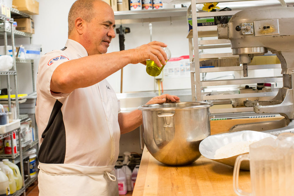 This photo shows John Arena pouring olive oil into a pan of dough.