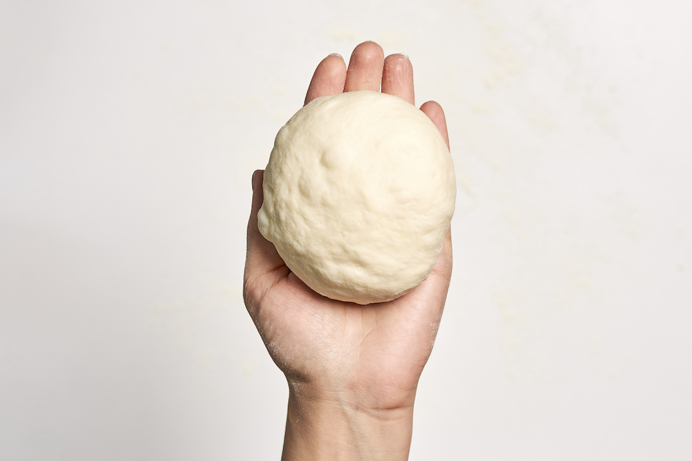 This photo shows a person's hand holding dough against a white background