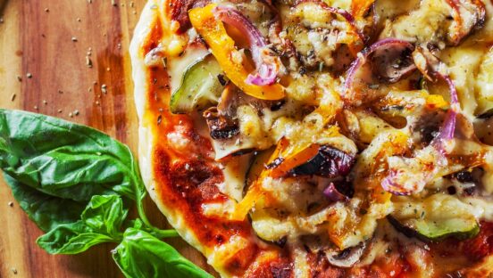 This photo shows a vegetarian pizza with Mozzarella cheese, grilled zucchini, mushrooms, red onion, pepper and fresh basil. Italian pizza on wooden table background.