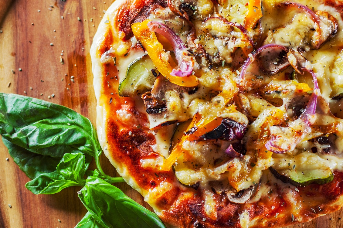 This photo shows a vegetarian pizza with Mozzarella cheese, grilled zucchini, mushrooms, red onion, pepper and fresh basil. Italian pizza on wooden table background.