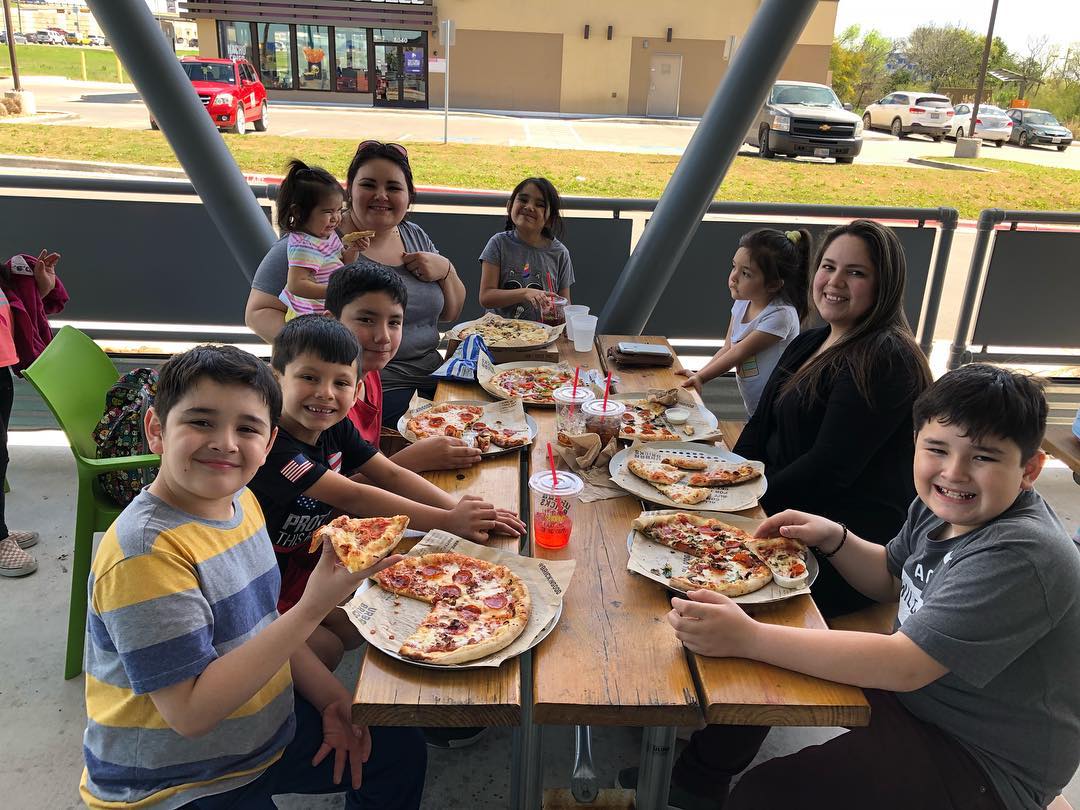 this photo shows a family, including kids, eating pizza on the patio at Urban Bricks Pizza