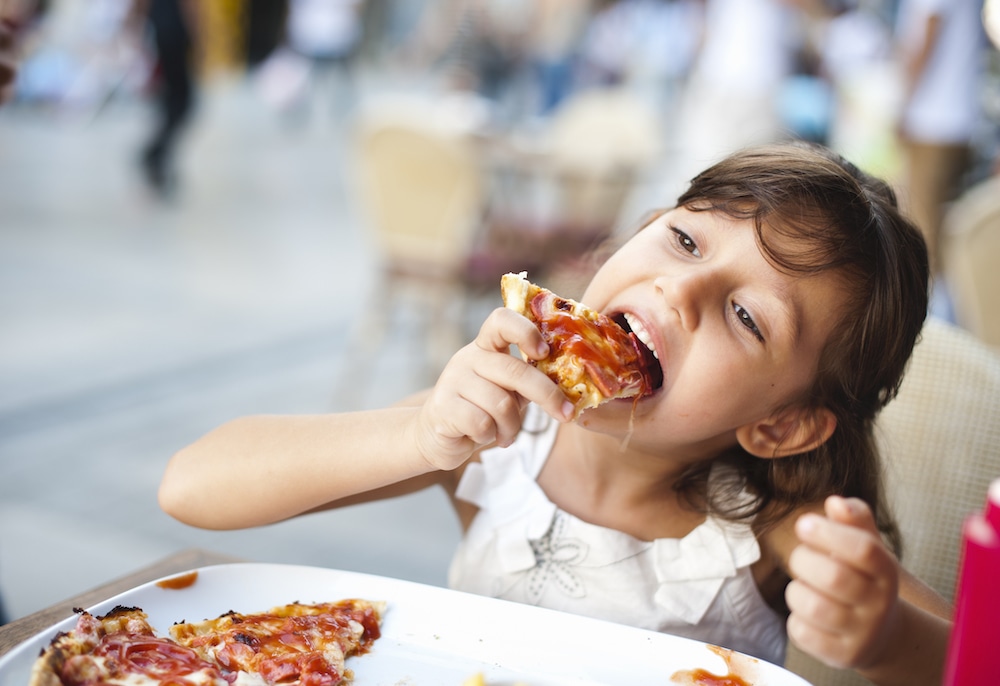 this photo of a little girl eating pizza illustrates increased customer satisfaction with chains like Domino's and Pizza Hut during the pandemic.