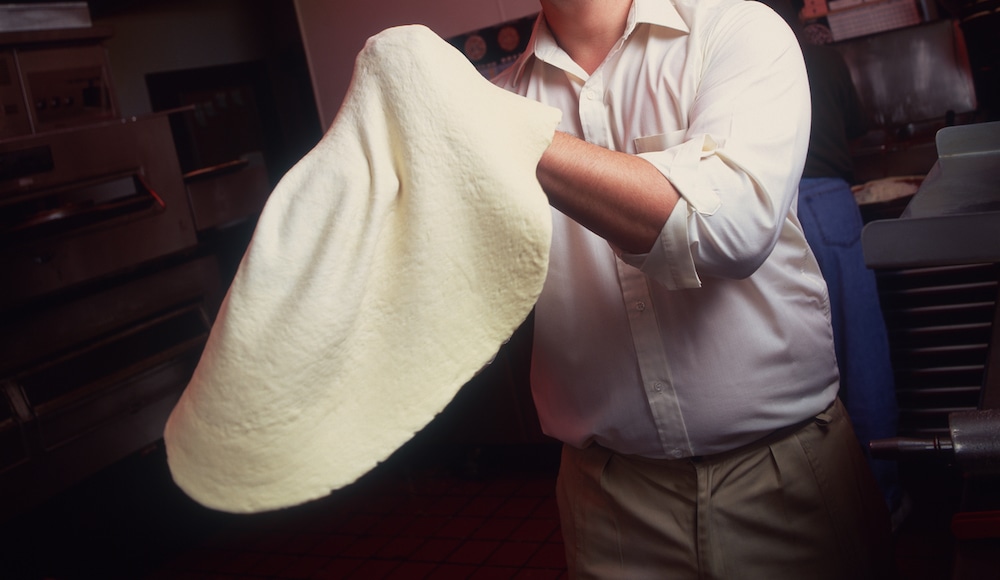 this photo shows a pizza maker stretching dough that is not too wet and sticky