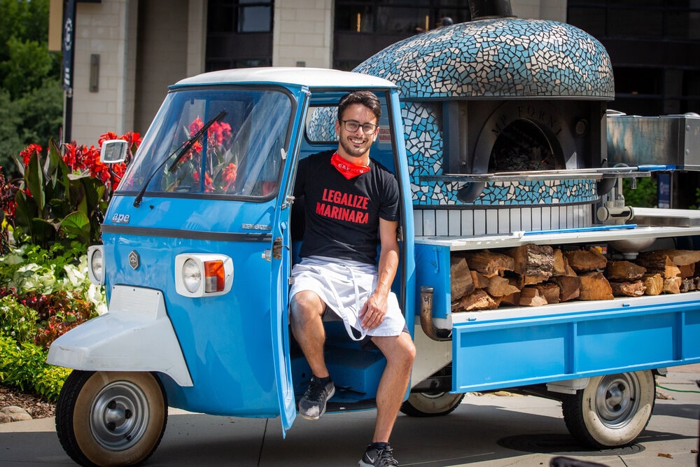 this photo shows Alessio Lacco in a blue three-wheeled Vespa scooter used by Atlanta Pizza Truck