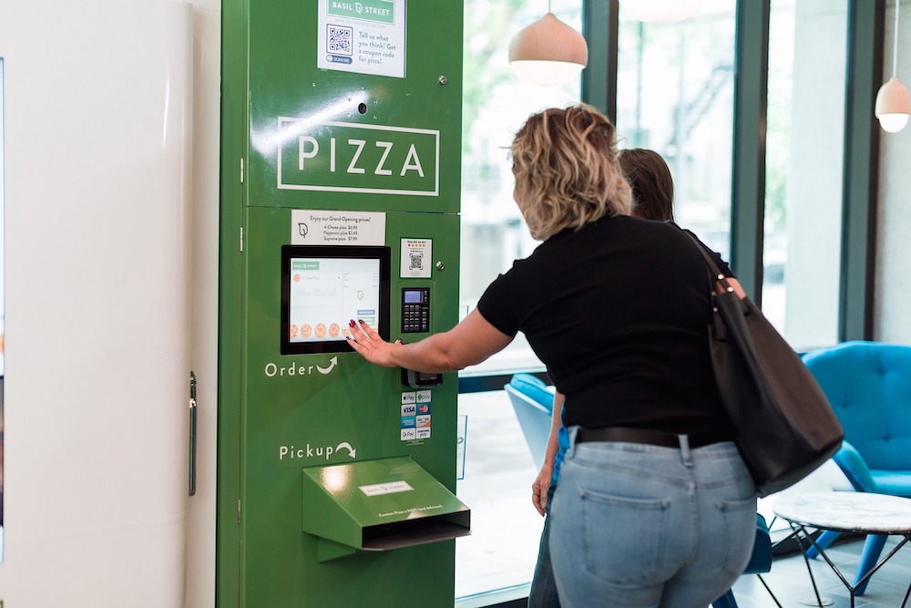 this photo shows a customer trying out one of Basil Street's automated pizza kitchens.