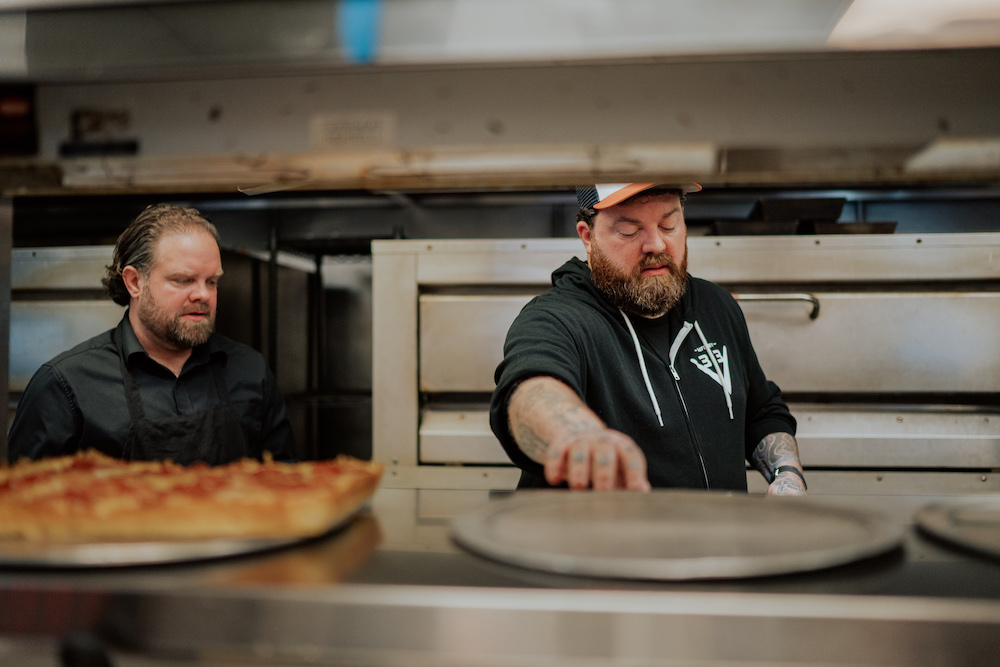 this photo shows the owners of Via 313 making a pizza in the kitchen