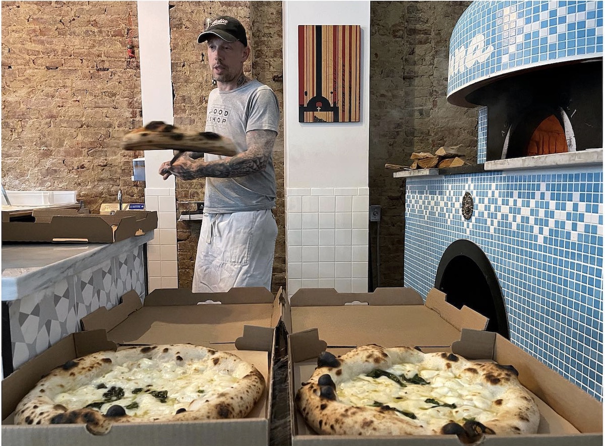 Anthony Mangieri, in a t-shirt and sporting tattoos on his arms, peels out a white pizza in the kitchen at Una Pizza Napoletana