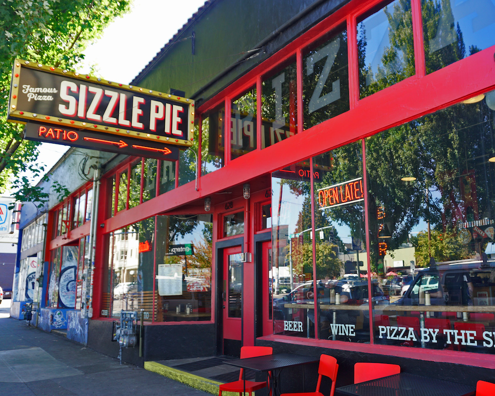 this photo shows the colorful exterior of Sizzle Pie's Central Eastside location in Portland, Oregon, including sharp reds, the Sizzle Pie sign and clear, bright windows