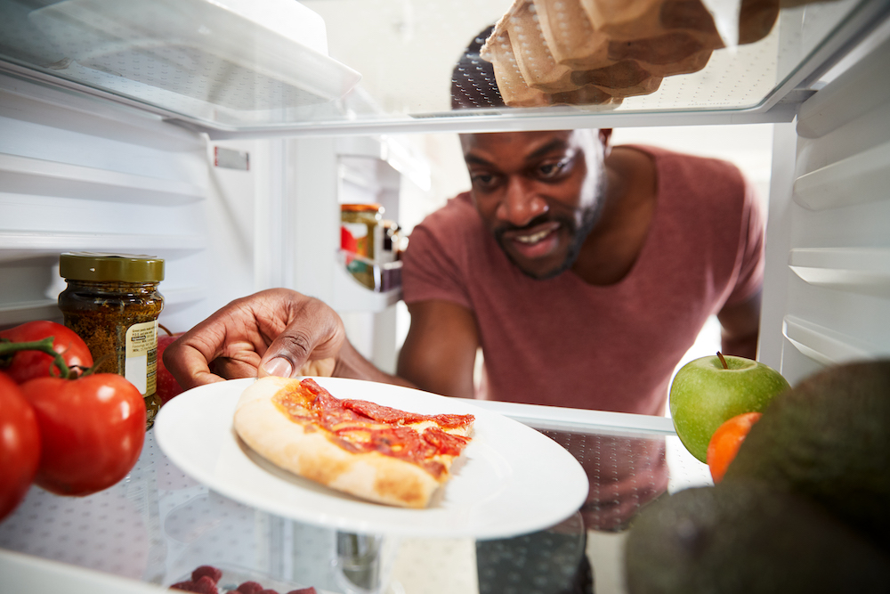 View Looking Out From Inside Of Refrigerator As Man Opens a refrigerator Door For Leftover Takeaway Pizza Slice