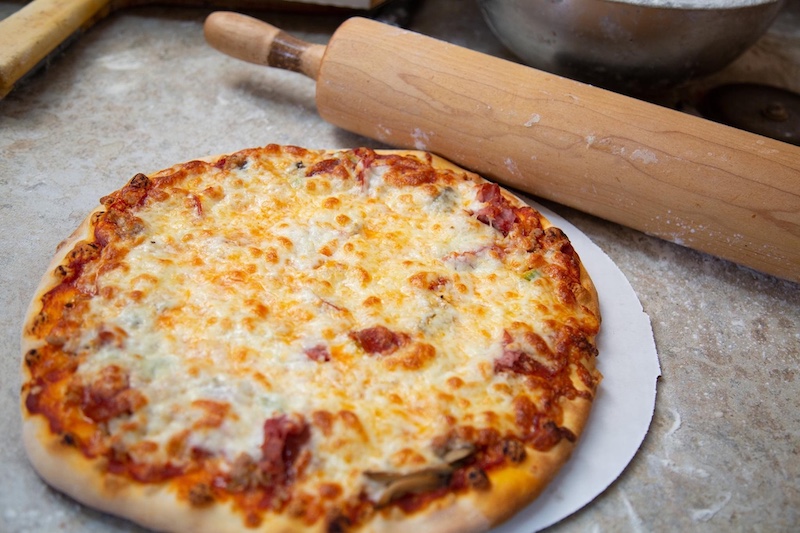 this photo shows a cheese pizza laid out on a paper sheet with a rolling pin next to it