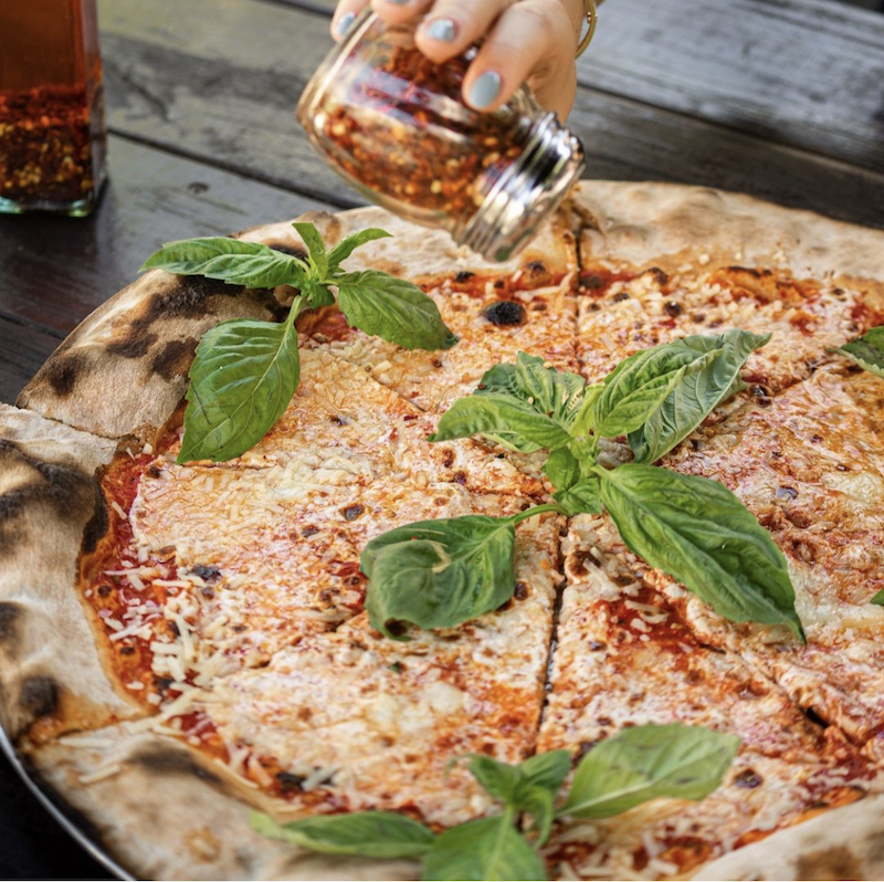 a hand shakes out some red pepper flakes on a cheese pizza at Lucali