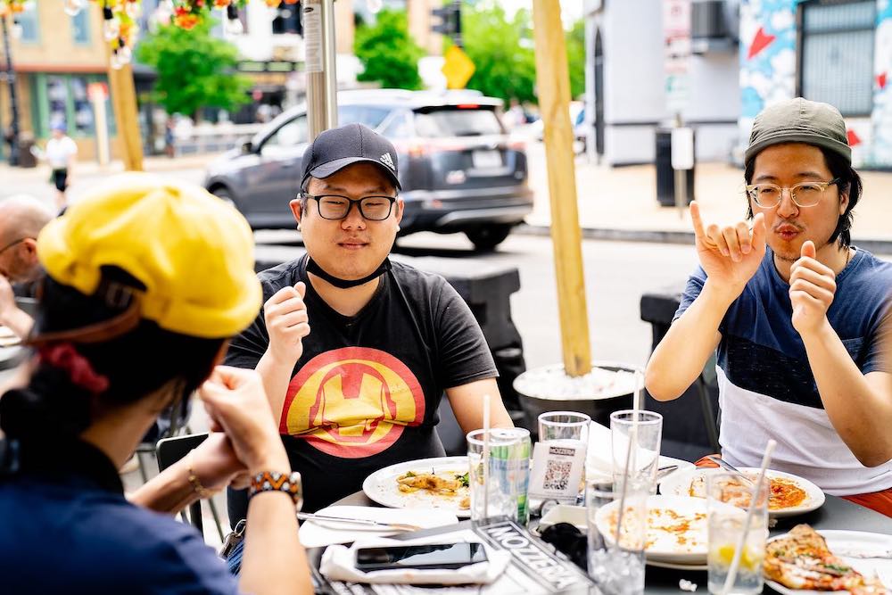 this photo shows three men speaking in American Sign Language while eating pizza on the patio at Mozzeria