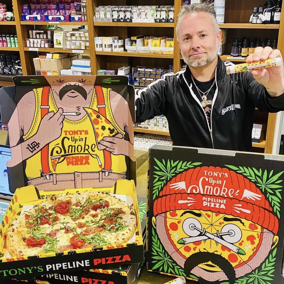 Tony Gemignani poses with a pizza box featuring Cheech-and-Chong influenced artwork - a man with a droopy mustache and a red pullover cap