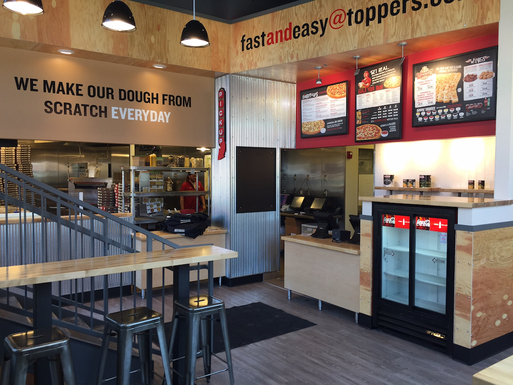 this is a photo of the interior of a Toppers Pizza location, including the menu board and walls with signs that read We Make Our Dough From Scratch Every Day and Fast and Easy@Toppers