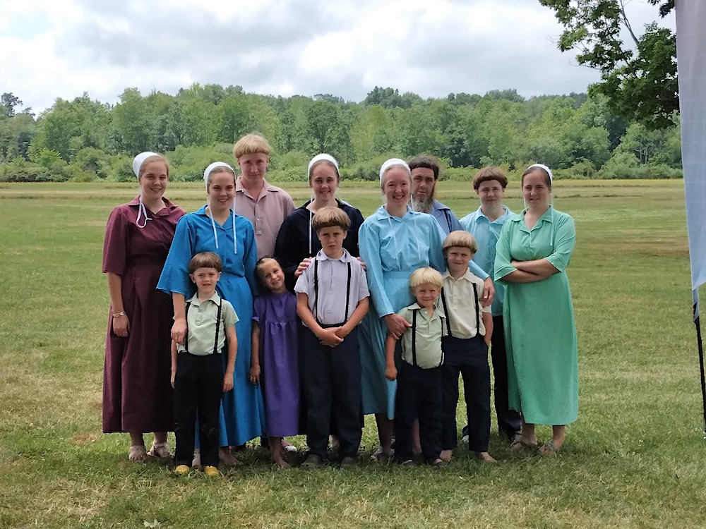 this photo shows a large Amish family with children of all ages in a pastoral setting in rural New York
