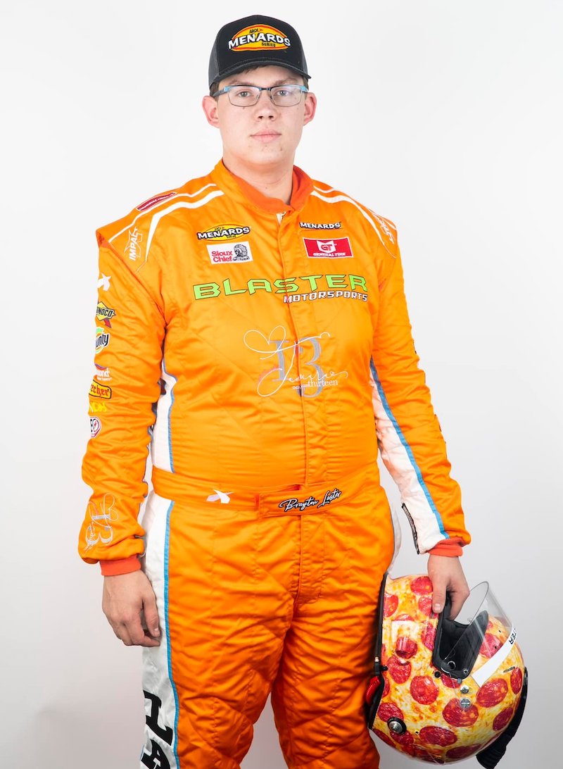 this photo shows Brayton Laster in his orange racing uniform, holding a pepperoni pizza-themed helmet at his side