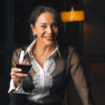 This photo shows Lisa Dahl holding a glass of wine and smiling. She is standing in a cozy, elegant dining room at one of her restaurants.