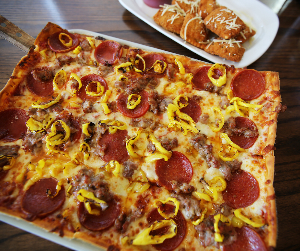this photo shows a delicious-looking, square-shaped pizza topped with pepperoni, Italian sausage and yellow peppers