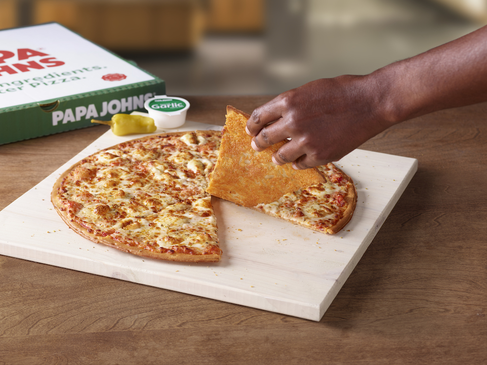 the hand of an African-American person flips one slice of a whole Crispy Parmesan pizza to reveal the cheesy bottom of the crust