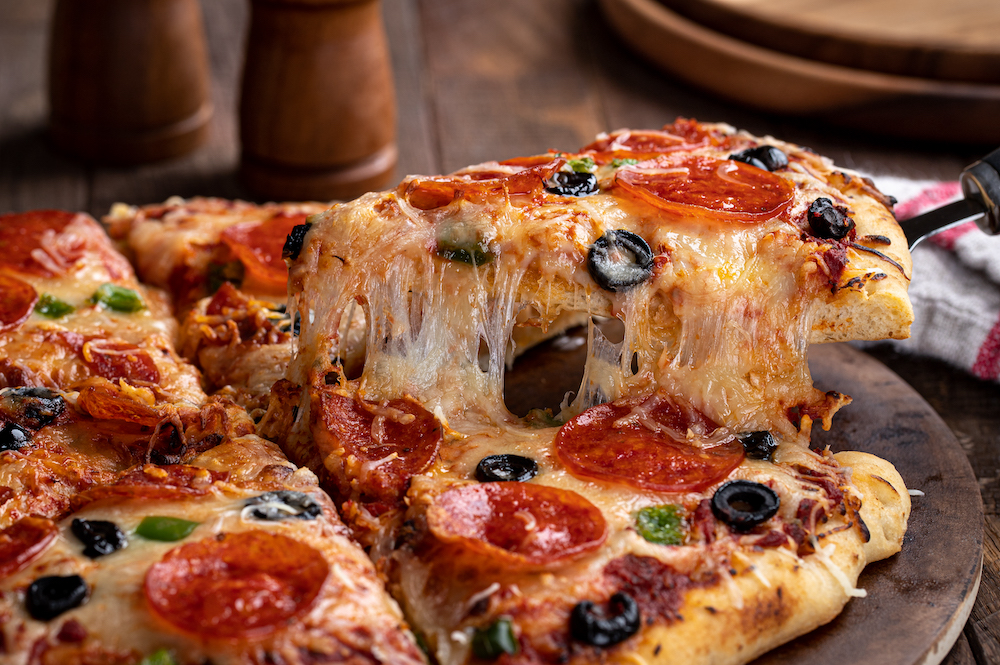 Slice of pizza with pepperoni, olives and green peppers on a serving utensil. Closeup of a cheese pull