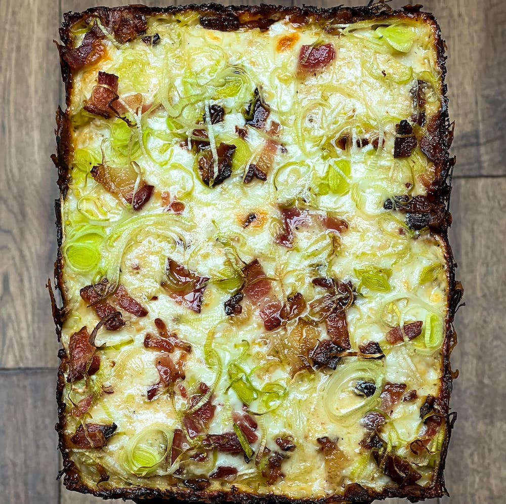 this is a photo of a square pie topped with bacon, leeks and pecorino cheese