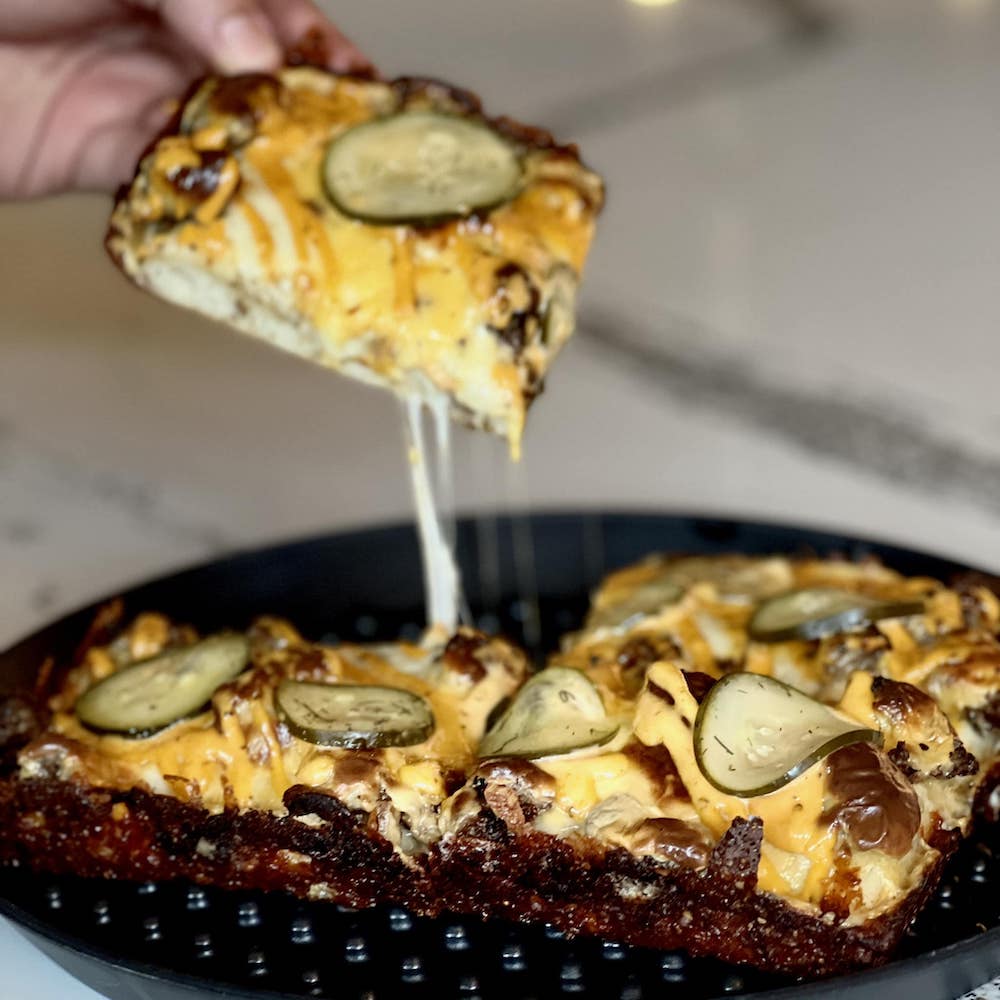 a slice of the Smashburger Pizza is lifted from a whole pie featuring beef, melty American cheese and pickles