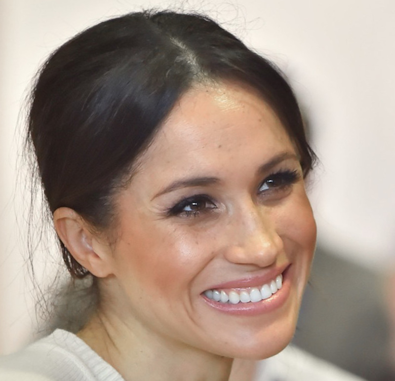 this is Meghan Markle with her hair pulled back, smiling and wearing a white blouse