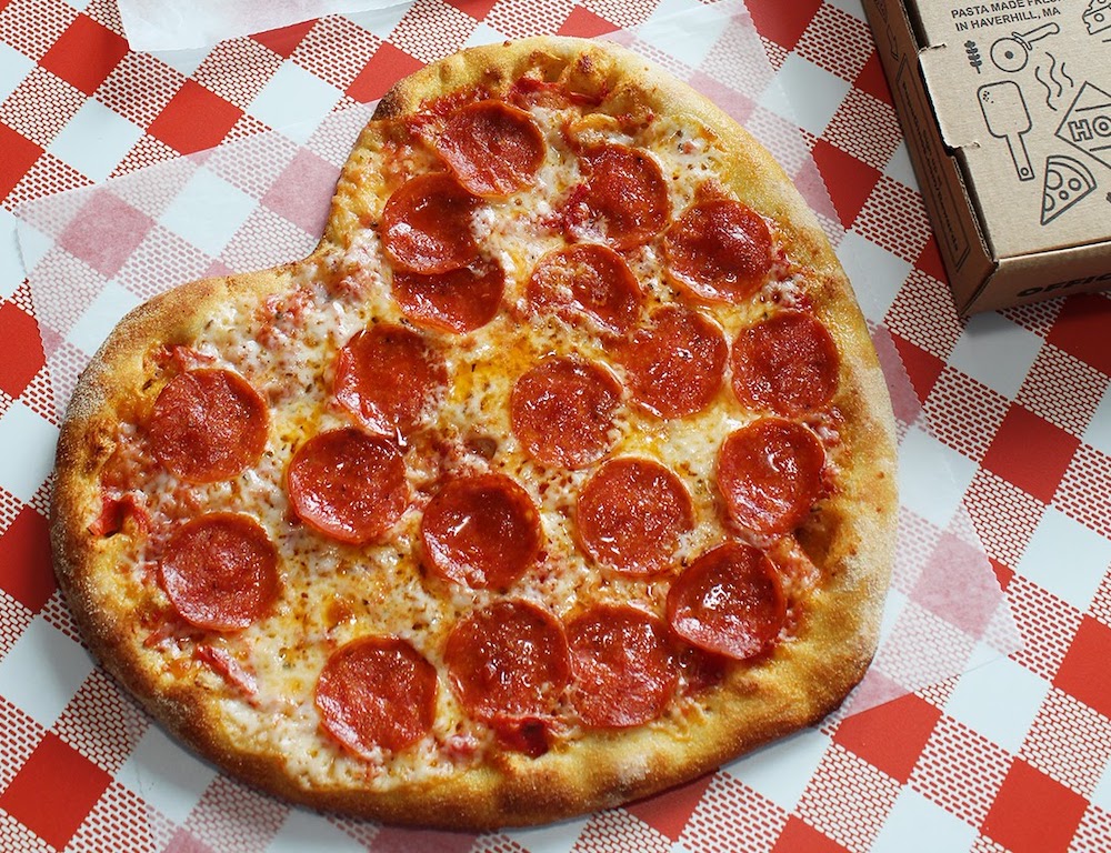 a heart-shaped pepperoni pizza placed on a checkerboard cloth