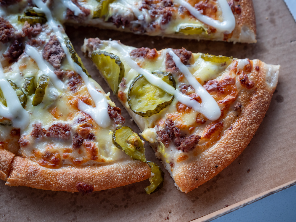 a pizza topped with pickles, meat and a drizzle of ranch dressing