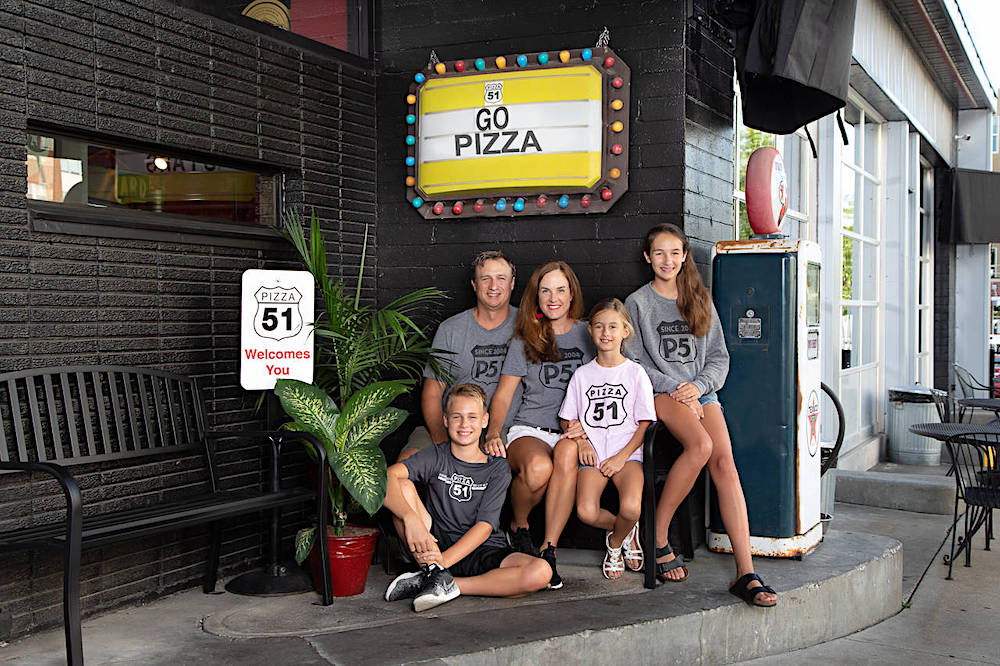 the owners of Pizza 51 and their three kids sit in front of a Pizza 51 sign outside the restaurant