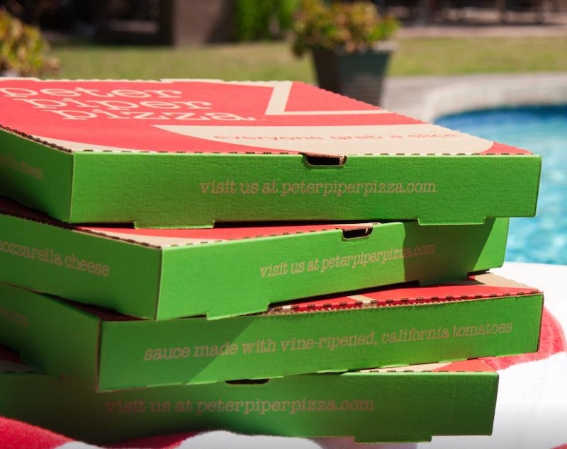 a stack of green and red Peter Piper Pizza boxes next to a swimming pool just barely visible on the right side