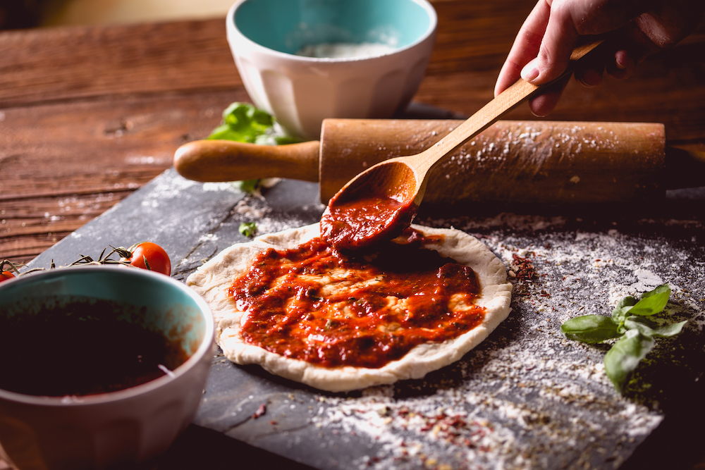 a wooden spoon is being used to ladle tomato sauce on a pizza crust