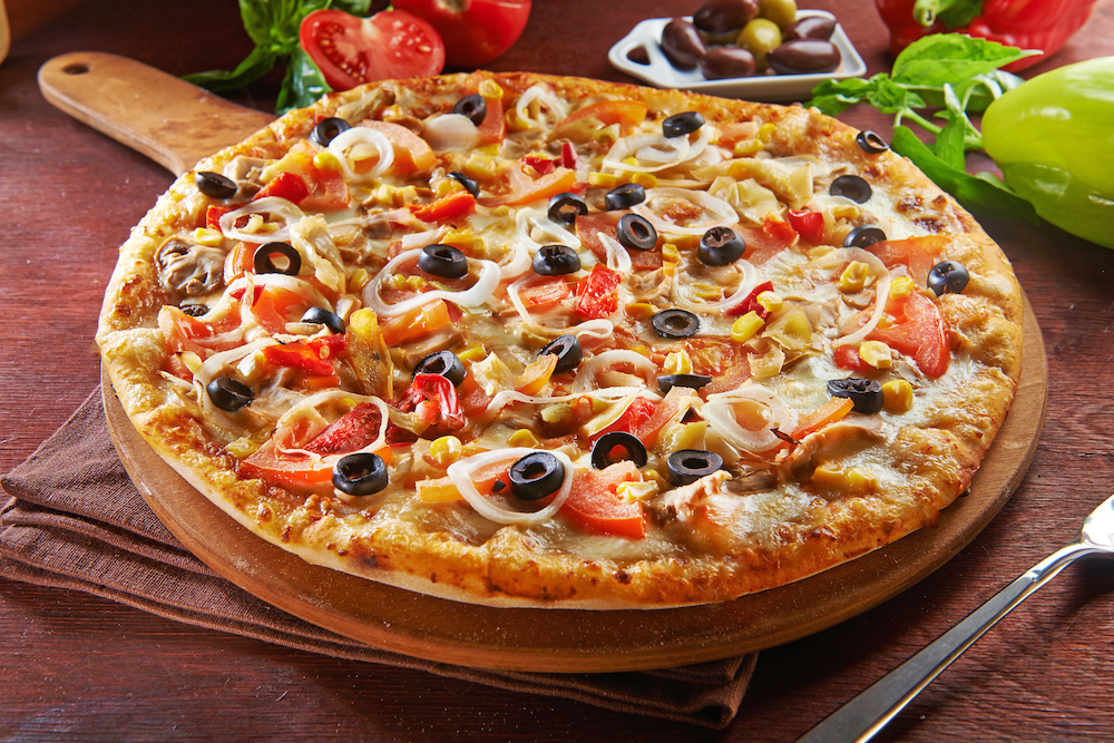 in a wooden platter, we see a beautiful pizza topped with a lot of healthy vegetables, including onions, mushrooms, black olives, red and orange peppers and corn