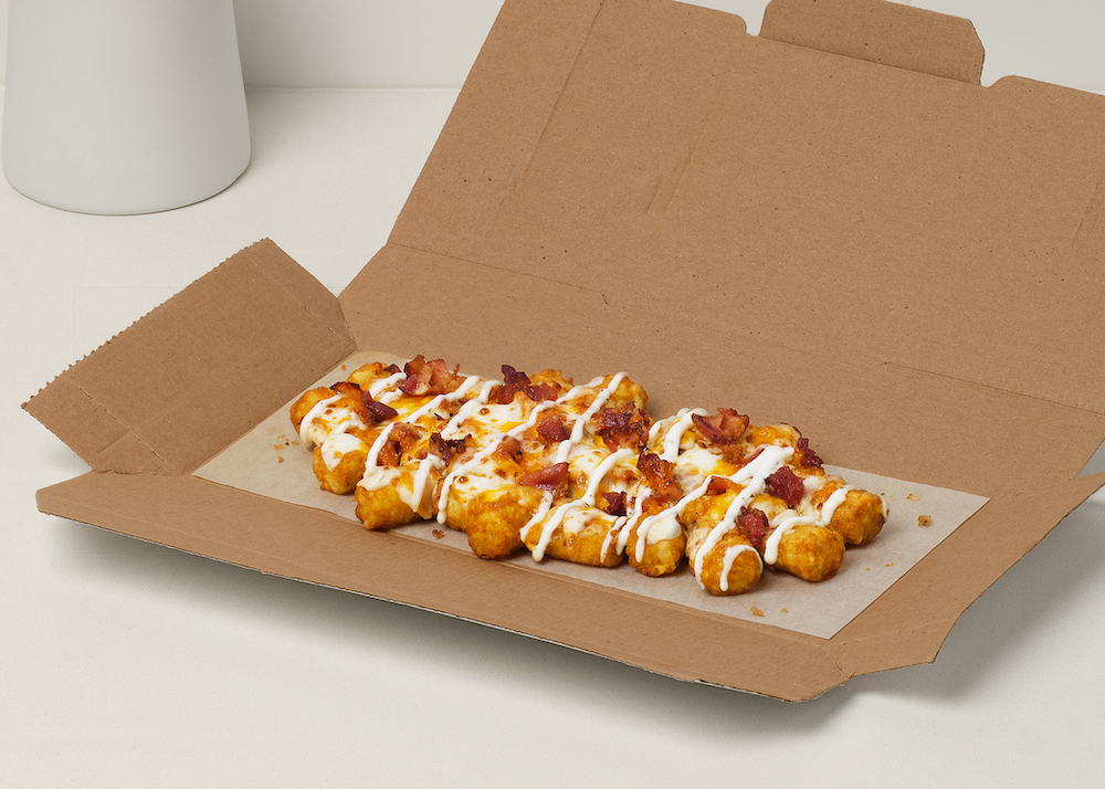 an order of loaded tots topped with cheddar cheese and bacon in a brown cardboard box