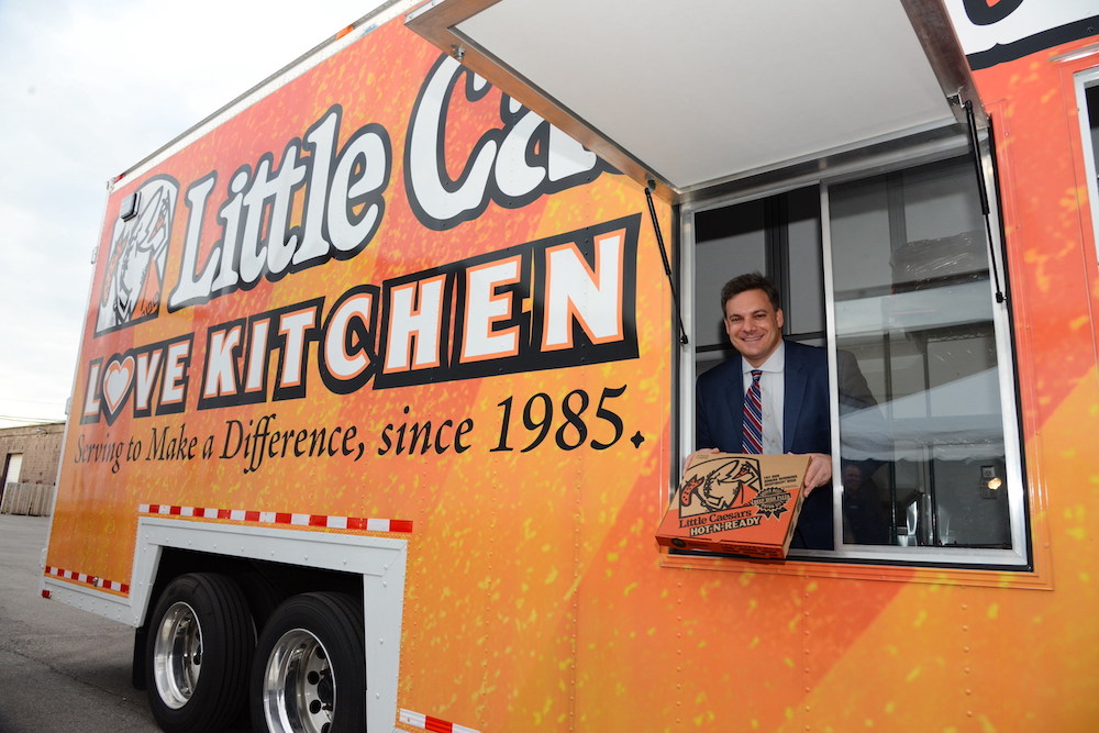 here we see Dave Scrivano of Little Caesars leaning out of the window of the Love Kitchen food truck and holding a pizza