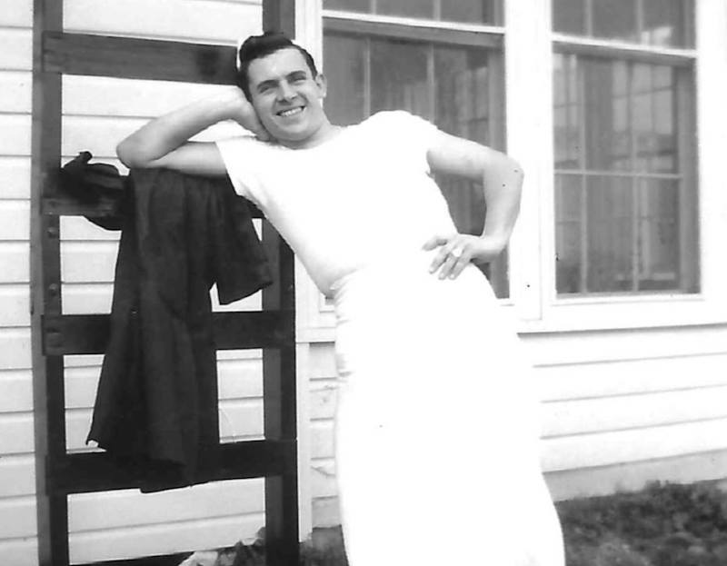 in this very old black-and-white photo we see Dominick Zuppardi, wearing a white shirt, pants and apron, leaning back against a ladder and smiling broadly