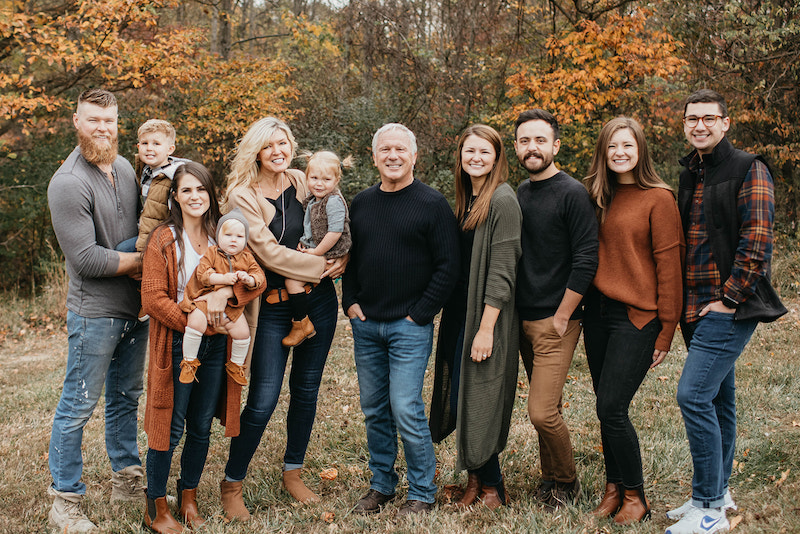 this photo shows the large extended Grote family lined up in an outdoor setting during the fall, with trees with golden leaves behind them.