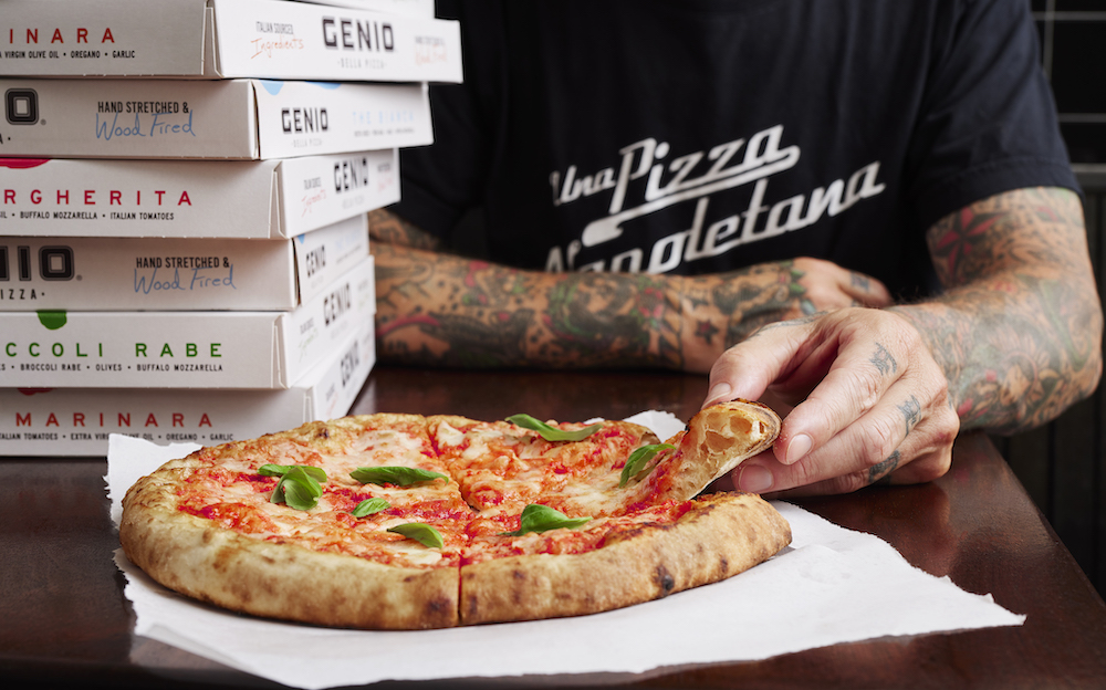 here is a closer shot of the Margherita pizza with Anthony Mangieri pulling out a slice. His arm is heavily tattooed. There's a stack of Genio Della Pizza boxes stacked nearby.