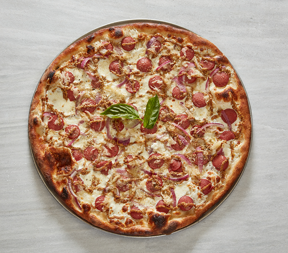 this shows a pizza topped with hot dog meat, red onions and other toppings