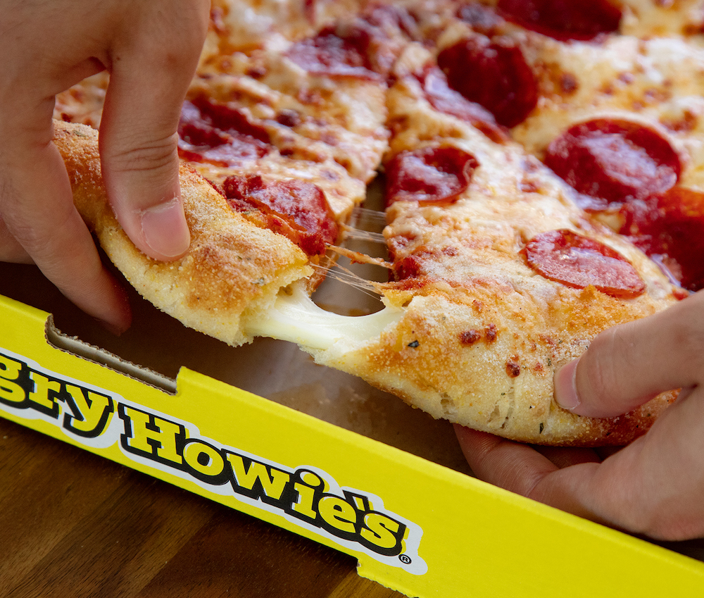 this photo shows a man's hand pulling out a slice of pizza with a cheese-stuffed crust