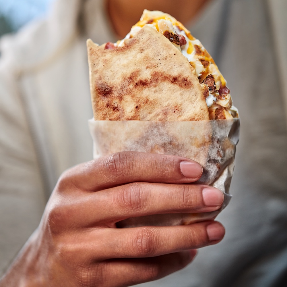 this photo shows a person's hand holding a pocket pie, which is a folded pizza crust stuffed with various toppings