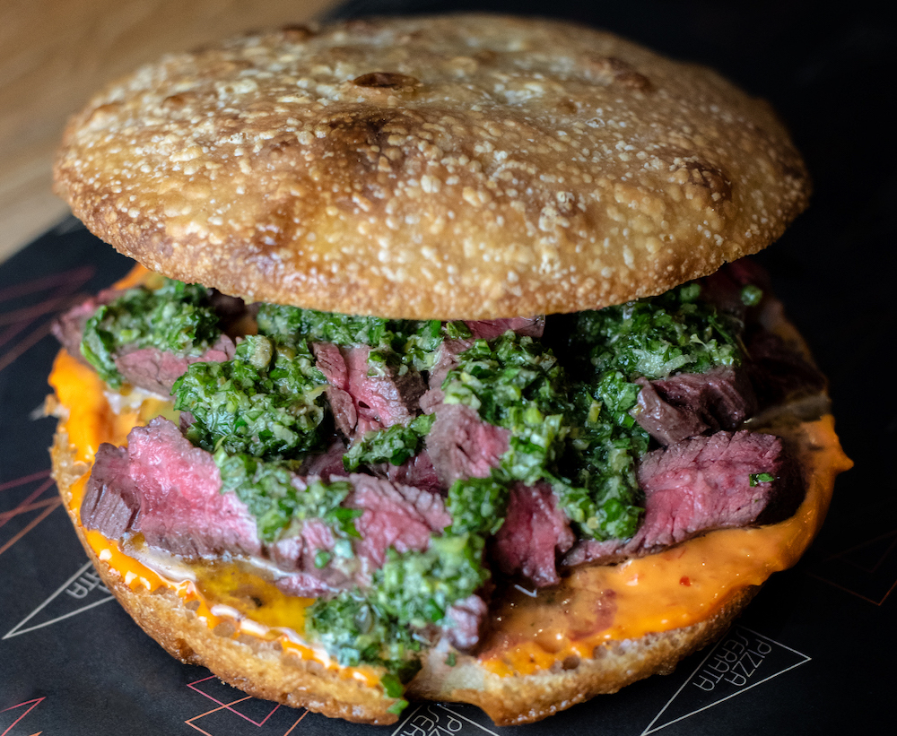 this photo shows a focaccia bread sandwich stuffed with medium rare skirt steak, a garlic aioli and salsa verde