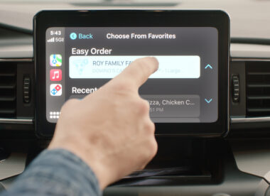this photo shows a man's hand touching the CarPlay touchscreen to order a pizza from Domino's