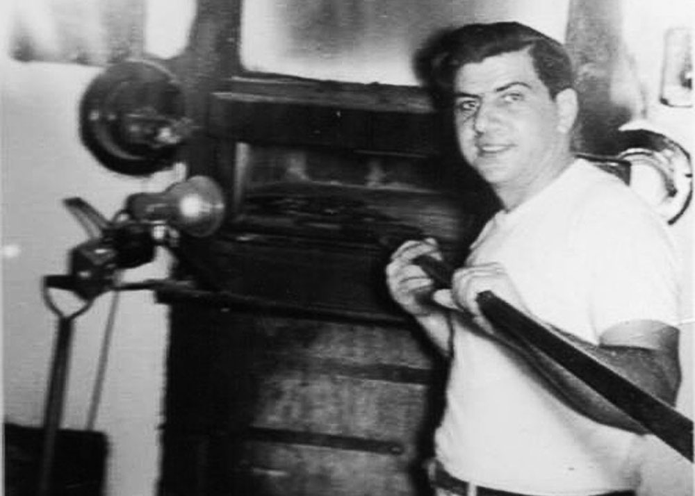 this vintage black and white photo shows Alfonso Jr. in a white t-shirt peeling a pizza into a large oven