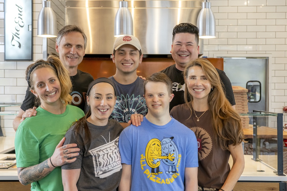 this photo shows MOD Pizza founders Scott Svenson and Ally Svenson along with a group of employees that include people who have benefited from its social programs to help justice-involved individuals and people with intellectual or developmental disabilities.