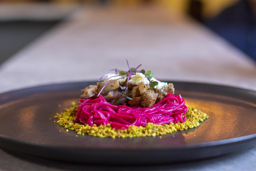 this is a side view of a pasta that's a purplish color sitting on a bed of chopped pistachios